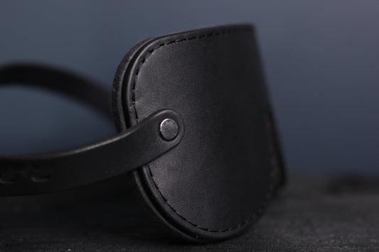 A side view of the black leather blindfold with black fixtures. 