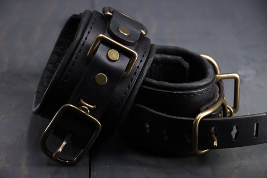 Closeup photograph of two black leather BDSM cuffs, with bronze fittings.