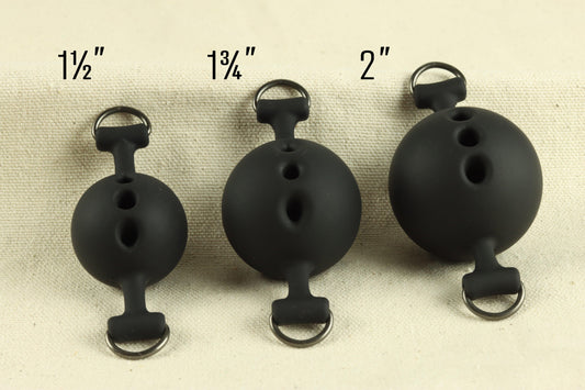Three different sized silicone ball gags are visible, increasing in size from left to right. Text over each ballgag reads, "one and one half inches," "one and three quarters inches," and "two inches." 