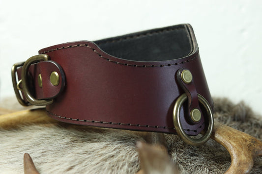 The locking bdsm posture collar is viewed from the front, resting on a bed of animal furs. It has a D ring on the side, right next to the locking buckle, and a ring on the front for easily attaching a lead or leash.