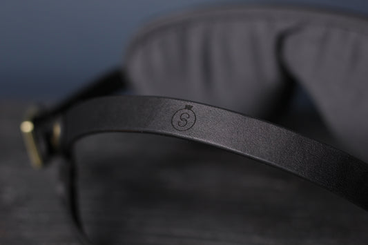 A closeup of the blindfold head harness strap in black leather, with the sabersmyth logo printed in the center.