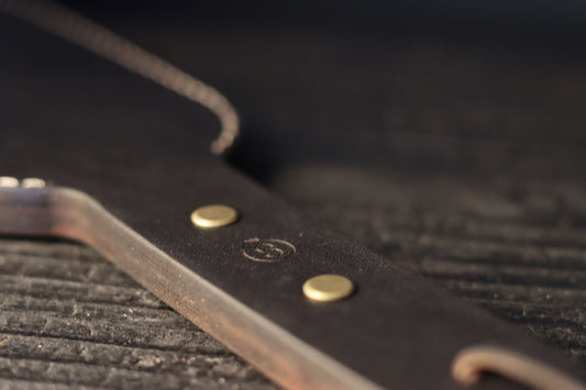 The black leather paddle is pictured, with a closeup on the handle. The leather is secured with two grommets in the handle. 