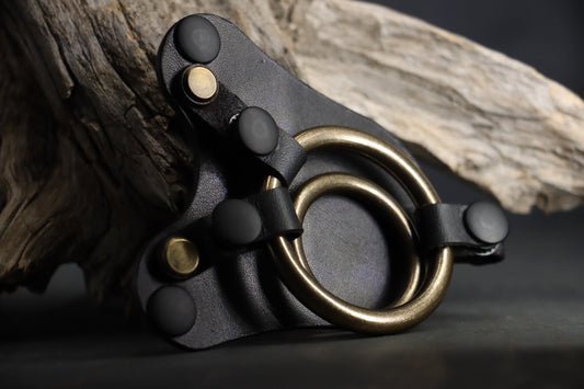 the leather strapon harness front plate designed for use with a dildo with balls rests against a piece of driftwood. 