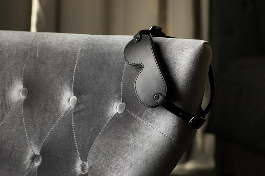 a black leather blindfold is draped over a grey tufted sofa. 