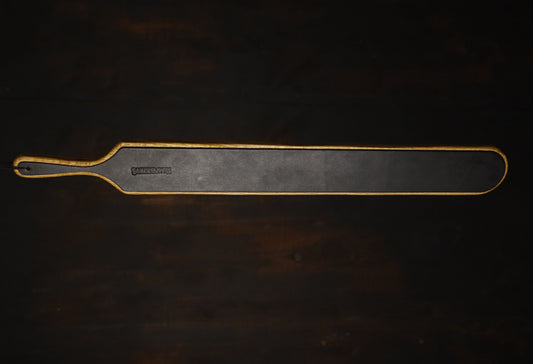 Image of the oak spaking paddle's leather side, displayed in full against a dark wood background. The paddle is about four times as long as the handle. 