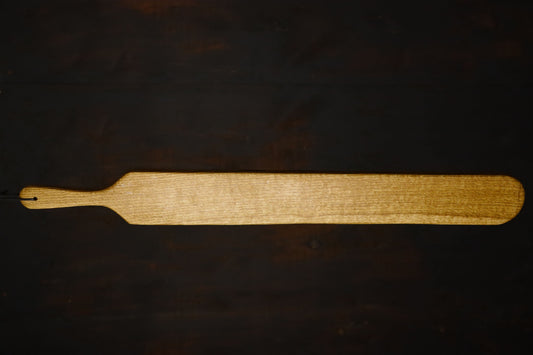Image of the oak spaking paddle's wood side, displayed in full against a dark wood background. The paddle is about four times as long as the handle.