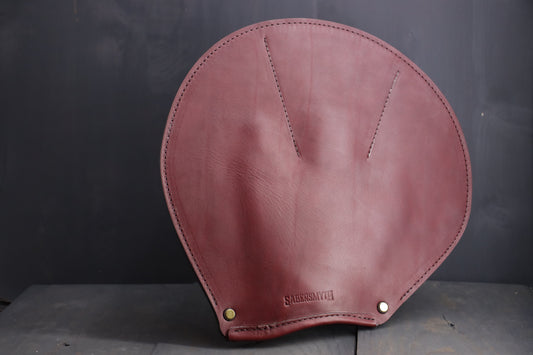 The leather spanking glove is pictured. It is a round piece of leather, with detailed stiching around the edges, and stitching to create a clear glove area for the wearer's hand.