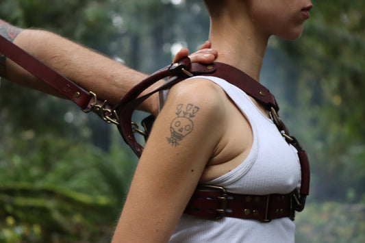 A person is viewed in profile wearing the harness, while another person pushes them away and pulls on the back of the harness, to show how the front part of the leather harness supports resistance. 